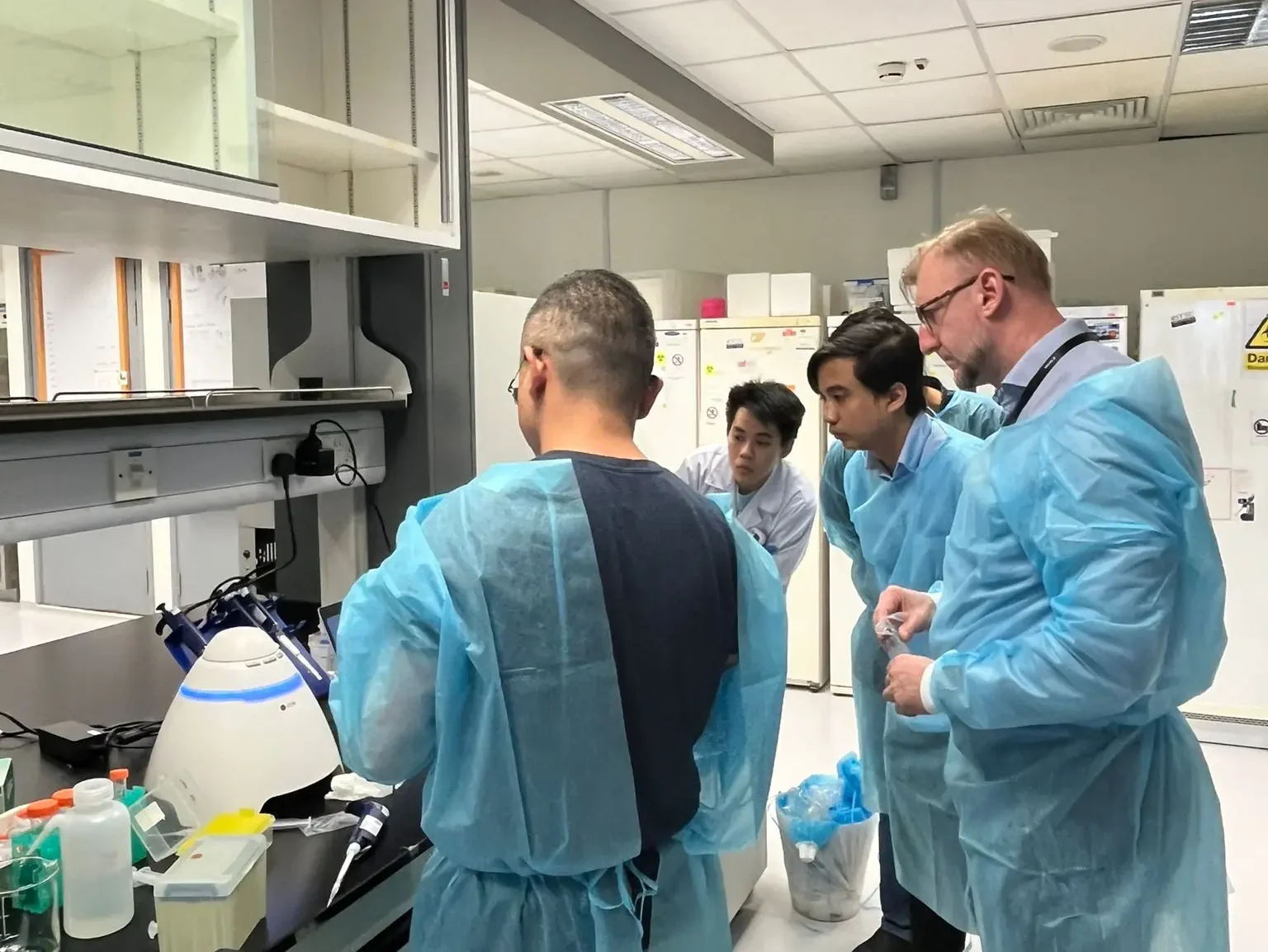 Dr Haoyu Xiong demonstrating Exoid nanoparticle analysis in a lab with attendees observing, all wearing blue lab gowns.